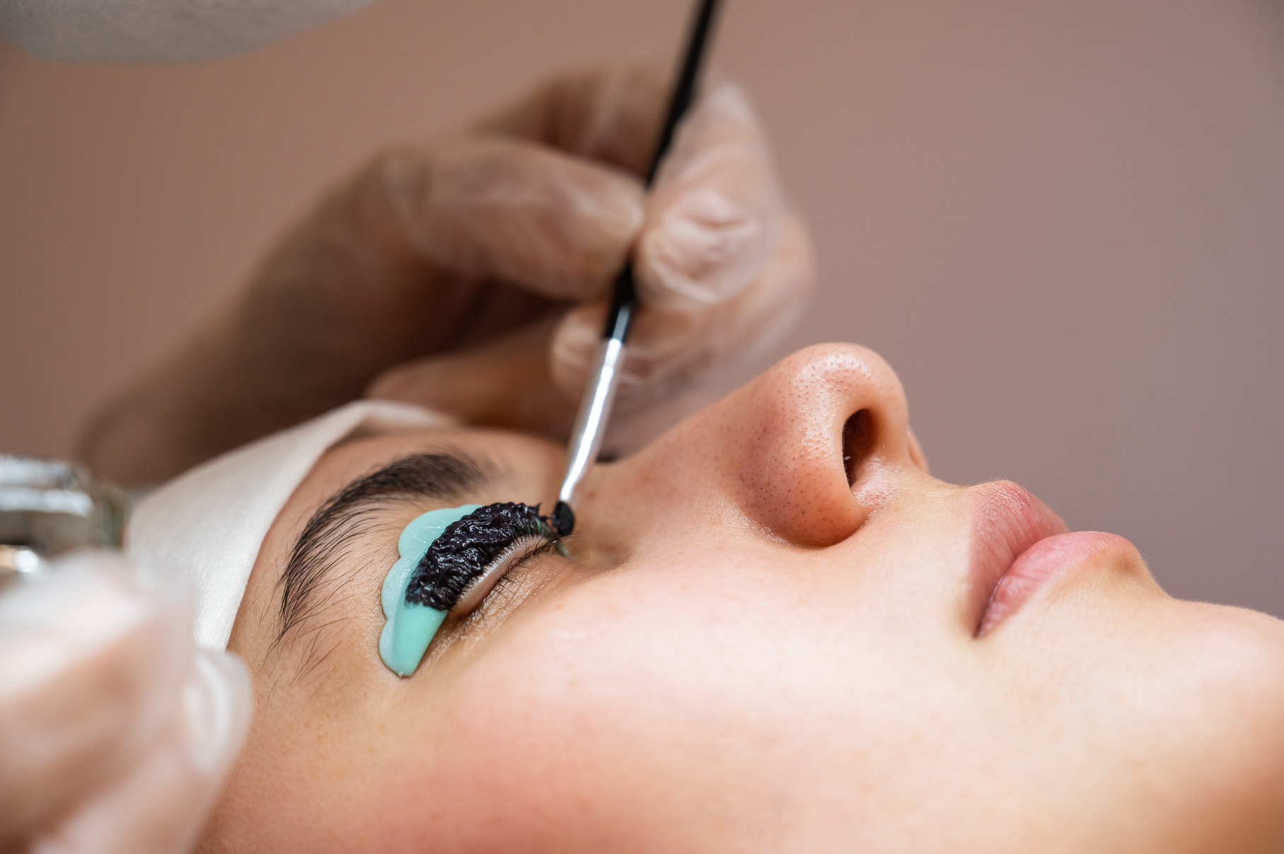 Close-up portrait of a woman on eyelash lamination procedure. The master applies tint to the eyelashes.